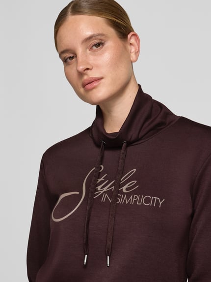 Frauenmodel trägt Regular Fit Sweatshirt aus reiner Modal-Mix Modell 'BANU' von Soyaconcept in Dunkelbraun, glatte Oberfläche, Schriftzug auf der Vorderseite, Nahaufnahme Oberkörper, Damen Sweatshirt von Soyaconcept.