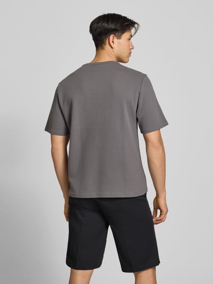 Männermodel trägt T-Shirt mit Label-Stitching von REVIEW in Grau mit Waffelstruktur, gerader Schnitt, Rückenansicht, Ganzkörperansicht Rückansicht.