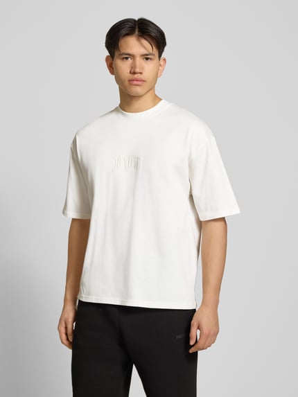Männermodel trägt T-Shirt mit Label-Stitching und Rundhalsausschnitt von REVIEW aus Reine Baumwolle, Relaxed-Fit, Rückenlänge 70 cm, Ganzkörperansicht von vorne.