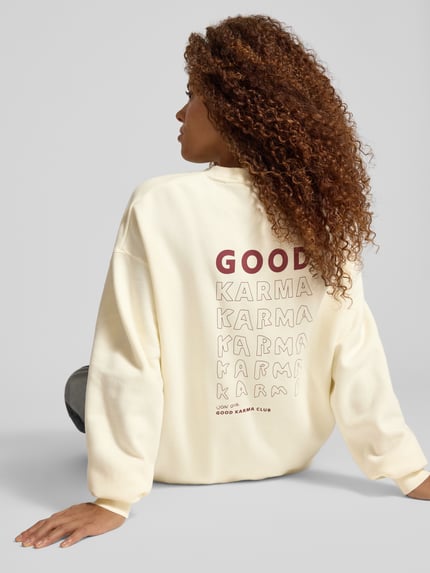Frauenmodel trägt Sweatshirt mit Rundhalsausschnitt Modell 'Good Karma' von OH APRIL in Creme mit rückseitigem Print, Oversized, Ganzkörperansicht Rückansicht. Baumwoll-Mix.
