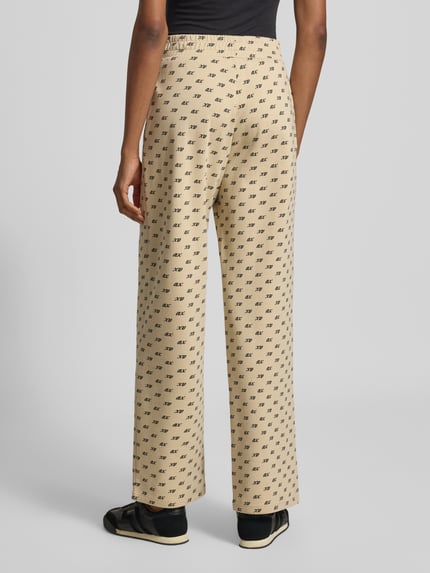 Frauenmodel trägt Wide Leg Sweatpants aus Baumwoll-Mix von Armani Exchange in Beige mit Allover-Logo-Print und gesmoktem Bund, Ganzkörperansicht Rückansicht.