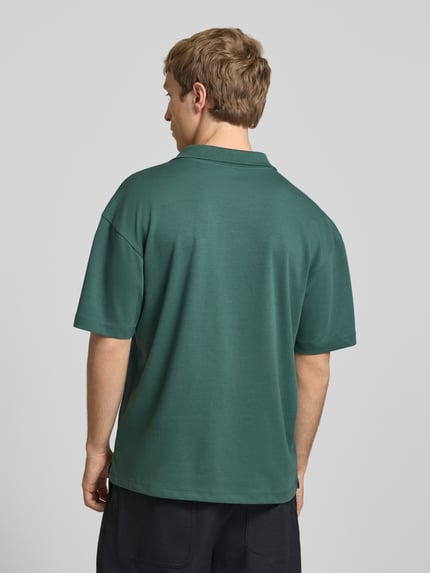 Männermodel trägt Boxy Fit Poloshirt aus Baumwoll-Mix Modell 'CASPIAN AIRLEX' von Only & Sons in einfarbigem Dunkelgrün, Jerseystruktur, Label Patch, Rückansicht Ganzkörperansicht