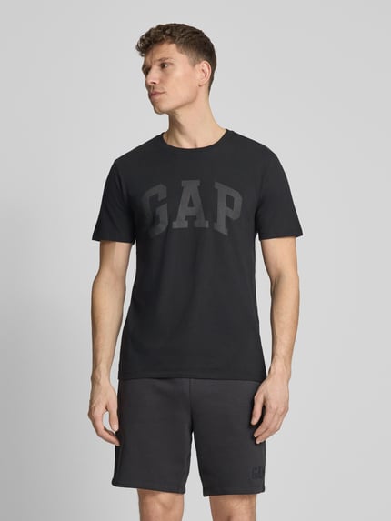 Männermodel trägt schwarzes Herren T-Shirt mit Logo und Rundhalsausschnitt von GAP aus reiner Baumwolle, Regular-Fit, Ganzkörperansicht von vorne. Rückenlänge bei Größe M: 72 cm.