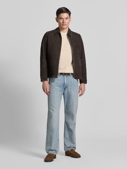 Männermodel trägt T-Shirt mit Rundhalsausschnitt und Label-Stitching von Gant in Beige, kombiniert mit Jeans und brauner Jacke, Ganzkörperansicht von vorne. Herren T-Shirt aus reiner Baumwolle im Regular Fit, Rückenlänge bei Größe M 69 cm.