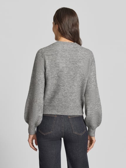 Frauenmodel trägt Strickjacke mit Zierknöpfen Modell 'VMHAZEL' von VERO MODA in grauer Melange-Optik mit Ballonärmeln, Ganzkörperansicht Rückansicht.