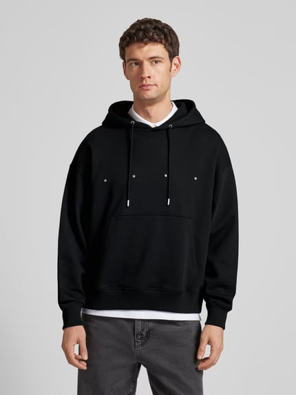 Męski model nosi Relaxed Fit Hoodie aus reiner Baumwolle Modell 'DOLAND' od HUGO, czarny, jednolity, z logo, długi rękaw, bawełna, widok z przodu, ujęcie całej sylwetki.