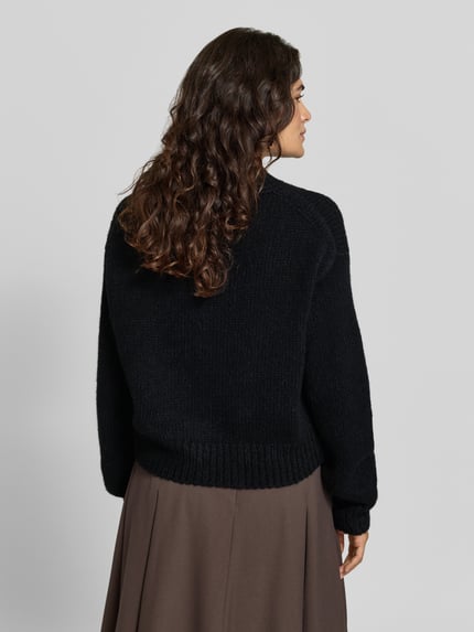 Modelka prezentuje sweter wełniany Pullover aus Wolle Alpaka mit Rippbündchen von MARC CAIN, krój regular fit, jednokolorowy, imitacja dzianiny, długość krótka, długie, obniżone rękawy z prążkowanym zakończeniem, okrągły dekolt, prążkowany dół, widok całej sylwetki z tyłu.