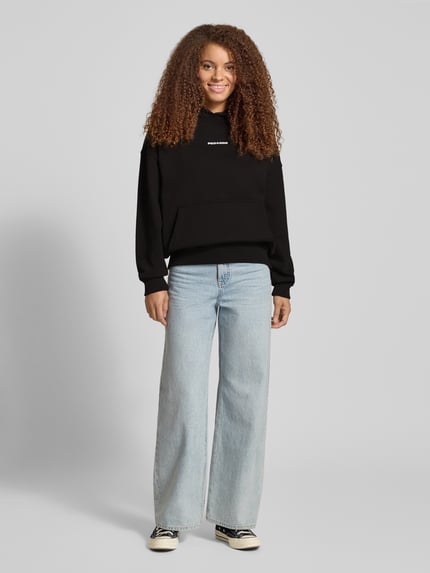 Frauenmodel trägt Oversized Hoodie mit Label-Stitching Modell 'CLARITA' von Pegador aus Baumwoll-Mix, schwarz, lockere Form, Ganzkörperansicht von vorne.