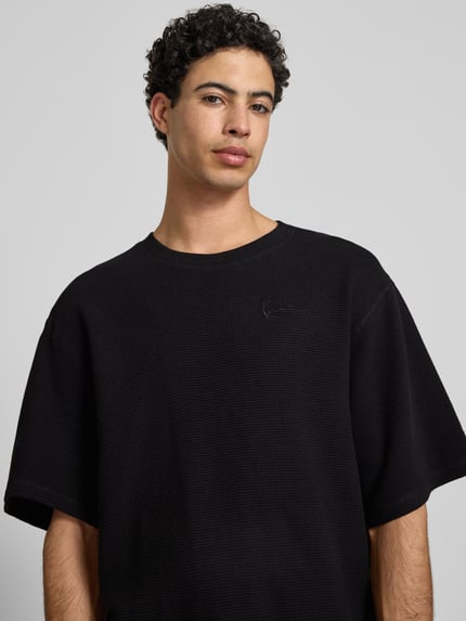 Männermodel trägt Relaxed Fit T-Shirt mit Strukturmuster von KARL KANI, Reine Baumwolle, Logo-Stitching, Rundhalsausschnitt, Nahaufnahme Oberkörper.