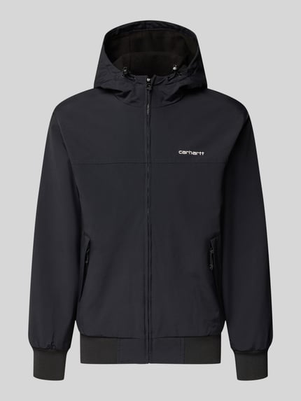 Produktfoto, Segeljacke mit Logo-Stitching und Kapuze von Carhartt Work In Progress in Schwarz, sichtbare Reißverschlüsse und gerippte Abschlüsse, seitliche Taschen, schlichte Form, glatte Textur