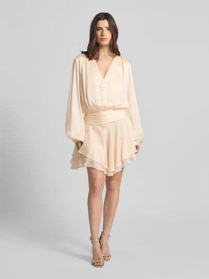 Frauenmodel trägt Minikleid mit kurzer Knopfleiste Modell 'MAGALI' von Guess, Taillierter Schnitt, V-Ausschnitt, Volantsaum, Cremefarben, Ganzkörperansicht von vorne.