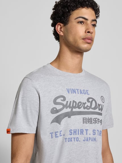 Männermodel trägt Relaxed Fit T-Shirt mit Logo-Stitching Modell 'Heritage' von Superdry, Baumwoll-Mix, Rundhalsausschnitt, Nahaufnahme Oberkörper.
