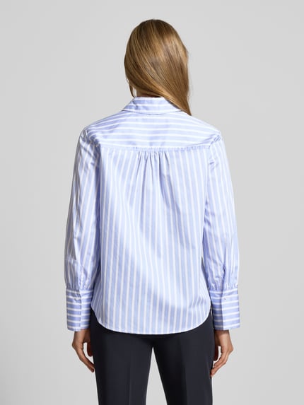 Frauenmodel trägt Regular Fit Bluse mit Knopfleiste Modell 'VICA' von Brax aus reiner Baumwolle, Hemdblusenkragen, Rückenlänge 65 cm, Ärmellänge 60 cm, blau-weiß gestreift, strukturierte Oberfläche, Ganzkörperansicht Rückansicht.