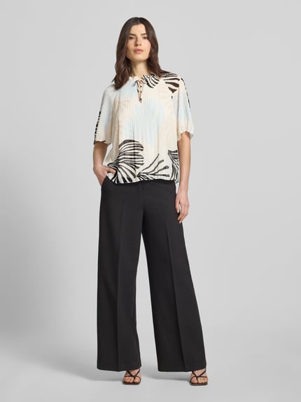 Vrouwenmodel draagt Regular Fit Blusenshirt in Plissee-Optik van s.Oliver BLACK LABEL, all-over motief, kraag met ruches, ronde hals, druppelvormige cut-out, vetersluiting, korte mouw, regular fit, plissés, kleuren crème en zwart, luchtige textuur, ganzekörperansicht van voren.