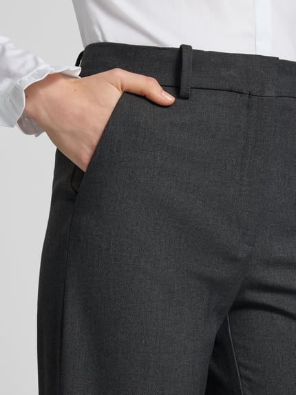 Frauenmodel trägt Straight Fit Hose mit Viskose-Anteil Modell 'Bergen' von MANGO in Dunkelgrau, glatte Textur, Nahaufnahme Oberkörper, elastischer Material-Mix, Bügelfalten sichtbar, Haken- und Reißverschluss.