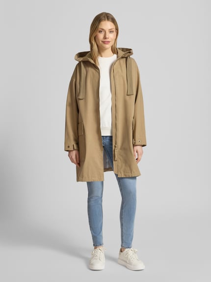 Frauenmodel trägt Regenmantel mit Kapuze und Zweiwege-Reißverschluss Modell 'UNA' von G-LAB in Beige, Gerader-Schnitt, Wasserdicht, Winddicht, Atmungsaktiv, Pattentaschen, Druckknopfverschluss, Ganzkörperansicht von vorne.