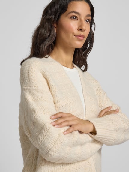 Frauenmodel trägt Strickjacke mit Strukturmuster Modell 'Wave' von FREE/QUENT in Creme, lockerer Sitz, wolliger Material-Mix, Nahaufnahme Oberkörper.