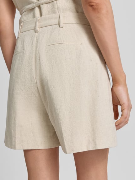 Frauenmodel trägt Shorts aus Ramie-Mix mit Biesen Modell 'Sega' von Neo Noir, beige, strukturierte Textur, Ganzkörperansicht Rückansicht, Damen Shorts, Ramie-Mix mit Baumwoll-Anteil, Straight Fit, Haken- und Reißverschluss, Bundweite bei Größe 36: 39 cm, Innenbeinlänge bei Größe 36: 11 cm.