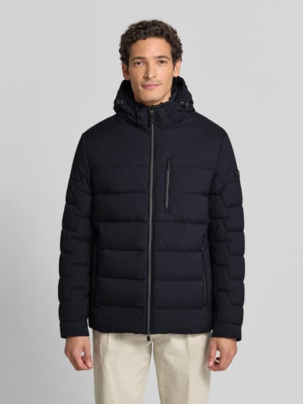 Männermodel trägt gewatteerd jack met capuchon, zwarte kleur, regular fit, Tweewegritssluiting, ritszakken, Steppjacke met Tweewege-Reißverschluss van bugatti, Heren, Ruglengte bij maat 50: 75 cm, Schouderbreedte bij maat 50: 49 cm, Borstwijdte bij maat 50: 60 cm, Mouwlengte bij maat 50: 67 cm, Ganzkörperansicht van voren.