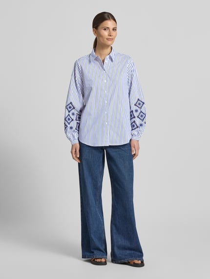 Kobiece model nosi Regular Fit Bluse mit Lochstickerei von Apricot, niebiesko-białe paski, mieszanka bawełny z dodatkiem streczu, haft angielski na rękawach, kołnierzyk koszulowy, listwa guzikowa, długość tyłu w rozmiarze S: 69 cm, długość rękawów w rozmiarze S: 61 cm, widok całej sylwetki z przodu.