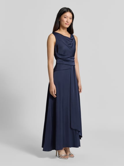 Frauenmodel trägt Abendkleid mit Wasserfallausschnitt von Rinascimento in Dunkelblau, fließender Stoff, Material-Mix mit Stretch-Anteil, taillierte Passform, Raffungen, Stoffgürtel, rückseitiger Reißverschluss, Ganzkörperansicht von vorne.