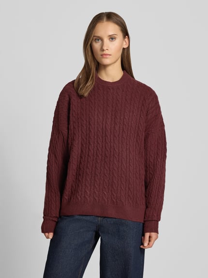Frauenmodel trägt Oversized Fit Strickpullover mit Zopfmuster von REVIEW, weinrot, elastischer Material-Mix, Jeans, Ganzkörperansicht von vorne.