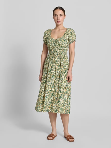 Vrouwenmodel draagt Midikleid aus Viskose mit Rüschenärmeln von Apricot in groen-geel bloemenpatroon, getailleerd model, zuiver viscose, ronde hals met ruches, vetersluiting, mouwen met ruches, smokdetail, ruglengte maat S 113 cm, borstwijdte maat S 29 cm, mouwlengte maat S 16 cm, geheelaanzicht van voren.