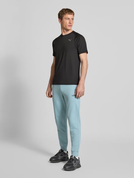 Męski model nosi T-shirt mit Label-Print von PUMA PERFORMANCE, mieszanka materiałów z dodatkiem streczu, krój regular fit, prążkowany okrągły dekolt, nadruk z logo, długość tyłu w rozmiarze M: 71 cm, całkowity widok z przodu.