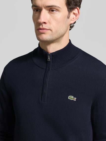 Männermodel trägt Pullover mit Troyerkragen BASIC KNIT TROYER von LACOSTE in Dunkelblau, Feinstrick, Logo-Patch, Nahaufnahme Oberkörper.