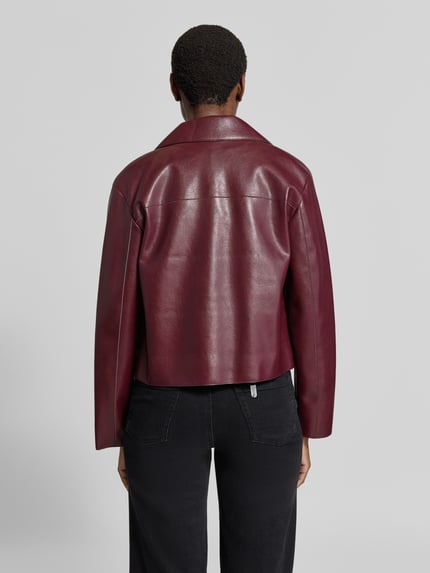 Frauenmodel trägt Jacke in Leder-Optik Modell 'SABINA' von MANGO in Dunkelrot, gerade Passform, glatte Oberfläche, Ganzkörperansicht Rückansicht. Rückenlänge 57 cm, Schulterbreite 44 cm, Brustweite 46 cm, Ärmellänge 60 cm.