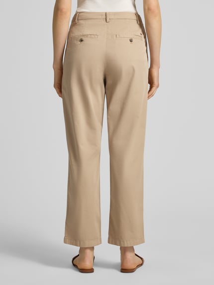 Kobiece model nosi Slim Fit Chino aus Baumwoll-Mix od Tommy Hilfiger, efekt: jednolity kolor, krój slim fit, mieszanka bawełny, wpuszczane kieszenie z boku i kieszenie z tyłu, szlufki na pasek, zapięcie na guzik i ukryty zamek błyskawiczny, widok całej sylwetki z tyłu.