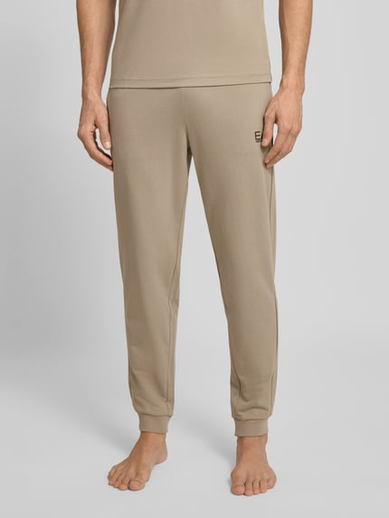 Männermodel trägt Sweatpants mit Logo und elastischem Bund von EA7 Armani im Regular-Fit aus Baumwoll-Elasthan-Mix, Nahaufnahme Unterkörper.