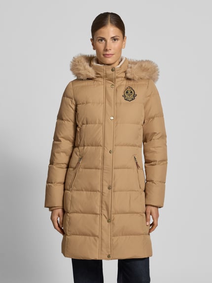 Frauenmodel trägt Steppmantel mit abnehmbarer Fellkapuze von LAUREN RALPH LAUREN in unifarbener Optik mit Logo-Detail, Reißverschlusstaschen, Knopf- und Reißverschluss, Kapuze und langen Ärmeln, Ganzkörperansicht von vorne.