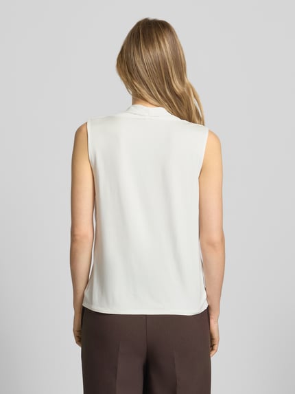 Frauenmodel trägt Top mit Wasserfall-Ausschnitt von comma aus Viskose-Elasthan-Mix in Creme, gerade Form, Ganzkörperansicht Rückansicht.
