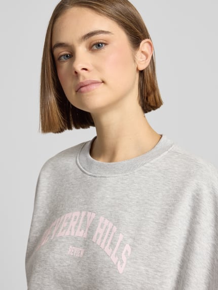 Frauenmodel trägt Sweatshirt mit Label-Print und Rundhalsausschnitt von Review aus Baumwoll-Mix im Relaxed-Fit, Nahaufnahme Oberkörper.