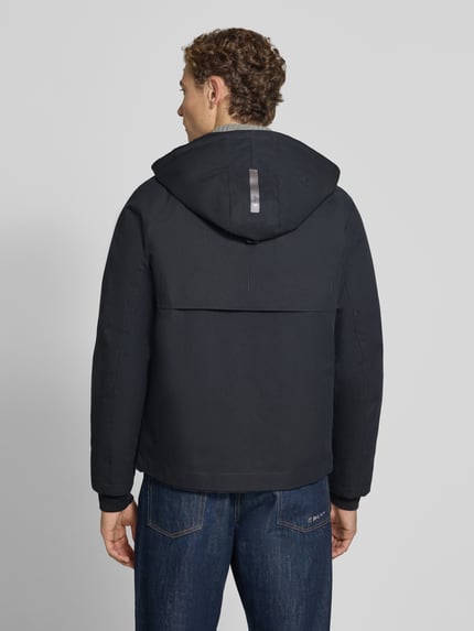 Männermodel trägt Jacke mit Kapuze Modell 'EDGE' von g-lab in Schwarz, strukturierter Stoff, gerade Passform, Ganzkörperansicht Rückansicht.