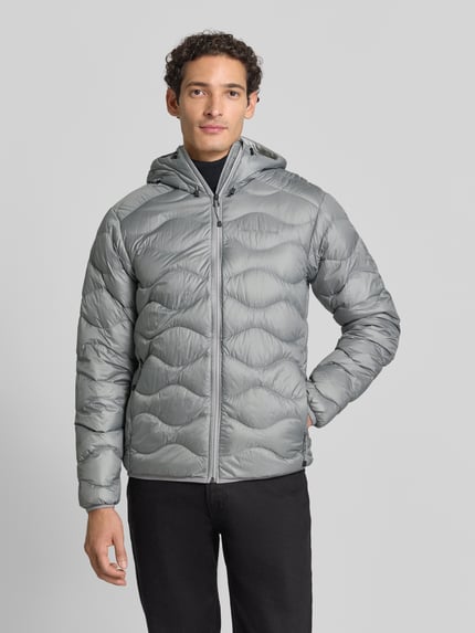 Männermodel trägt Slim Fit Steppjacke mit Kapuze Modell 'Helium' von Peak Performance in Grau, glatte Struktur, Ganzkörperansicht von vorne. Rückenlänge, Schulterbreite, Brustweite und Ärmellänge wie im Kontext beschrieben.