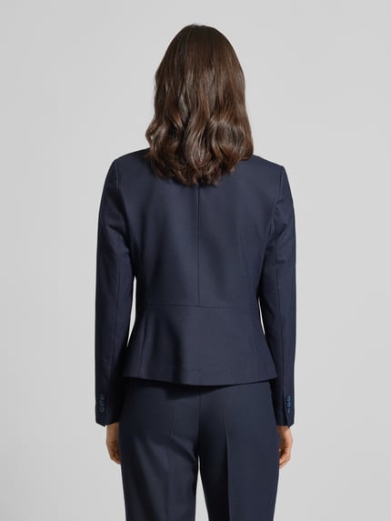 Kobiece modelka nosi Slim Fit Blazer mit Reverskragen von More & More, mieszanka materiałów z dodatkiem wiskozy, zapięcie na guzik, kieszenie z wypustkami, długość tyłu w rozmiarze 36: 57 cm, szerokość w rozmiarze 36: 46 cm, długość rękawów w rozmiarze 36: 64 cm, widok całej sylwetki z tyłu.