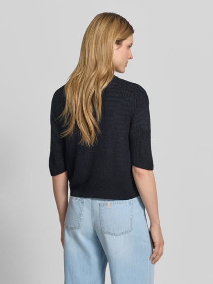 Frauenmodel trägt Cardigan mit V-Ausschnitt und 3/4-Arm von More & More in Schwarz, Relaxed-Fit, grobe Struktur, Rückenlänge 48 cm, 3/4-Arm, Ganzkörperansicht Rückansicht.