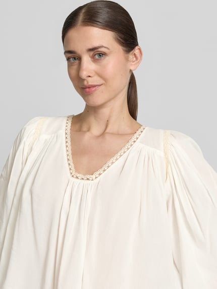 Frauenmodel trägt Cropped Bluse mit 3/4-Arm Modell 'ISMARA' von Drykorn aus Baumwoll-Viskose-Mix in Creme mit V-Ausschnitt, Nahaufnahme Oberkörper.