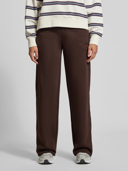 Frauenmodel trägt Sweathose mit geradem Bein von REVIEW in Dunkelbraun, Baumwoll-Mix, elastischer Bund, Logo-Print, Ganzkörperansicht von vorne.