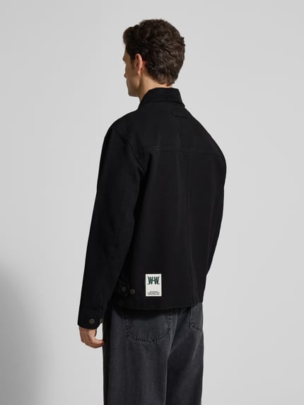 Männermodel trägt schwarze Jacke mit Zweiwege-Reißverschluss Modell 'Bo' von Wood Wood aus Baumwolle, lockerer Schnitt, Rückenansicht.