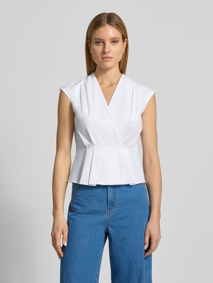 Vrouwenmodel draagt Regular Fit blouse met plooien model 'Bazar' van Marella, katoenmix, mouwloos design, V-hals, wikkellook, ruglengte bij maat 36: 55 cm, kleur wit, structuur glad, vooraanzicht volledige lichaamsopname.