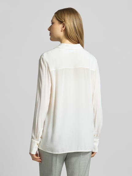 Frauenmodel trägt Relaxed Fit Hemdbluse aus reiner Viskose von Comma, weiß, mit Hemdblusenkragen, gelegte Falten, langärmelig, Rückenlänge 62 cm, Ärmellänge 62 cm, Ganzkörperansicht Rückansicht.