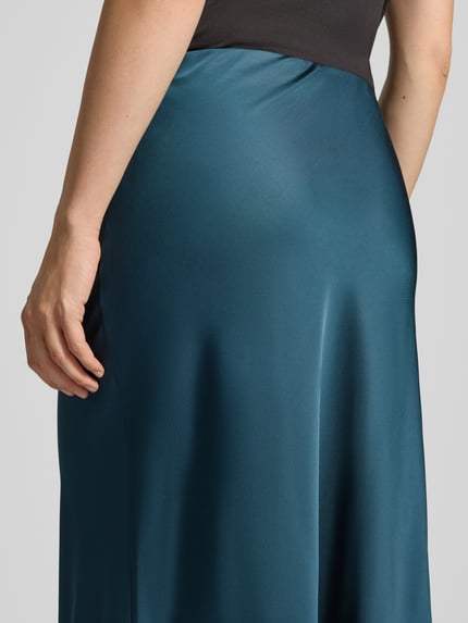 Frauenmodel trägt Maxirock mit elastischem Bund von COMMA, schimmernder Viskose-Mix in Petrol, A-Linie, Detailaufnahme Rückansicht.