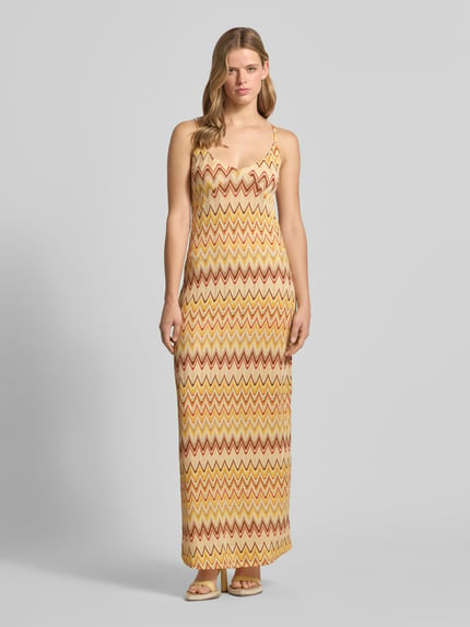 Vrouwenmodel draagt Maxikleid im Allover-Look van Gina Tricot, materiaalmix met stretch, recht model, V-hals, spaghettibandjes, all-over look, lichtgeel en bruin zigzagpatroon, ruglengte maat S 150 cm, borstwijdte 32 cm. Ganzkörperaanzicht van voren.