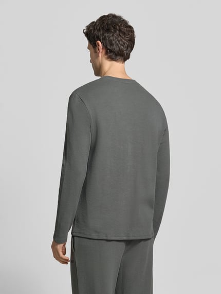 Männermodel trägt Longsleeve mit Logo-Schriftzug von BOSS in unifarbener Optik, langarm, Rundhals, abgerundeter Rumpfabschluss, Ganzkörperansicht Rückansicht.