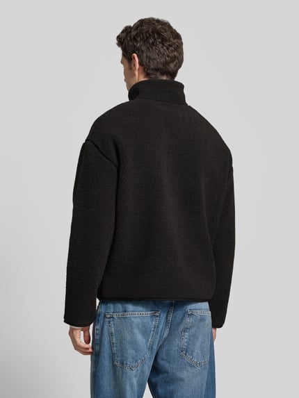 Männermodel trägt Bomberjacke mit Logo-Detail von LACOSTE in Schwarz, Stehkragen, elastische Bündchen, unifarbene Optik, Ganzkörperansicht Rückansicht.