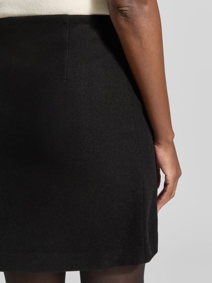 Frauenmodel trägt Ausgestellter Mini-Rock mit Nahtreißverschluss Modell 'FORTUNEALLISON' von VERO MODA, schwarze Farbe, glatte Textur, Ganzkörperansicht Rückansicht. Damen Mini-Rock von VERO MODA.