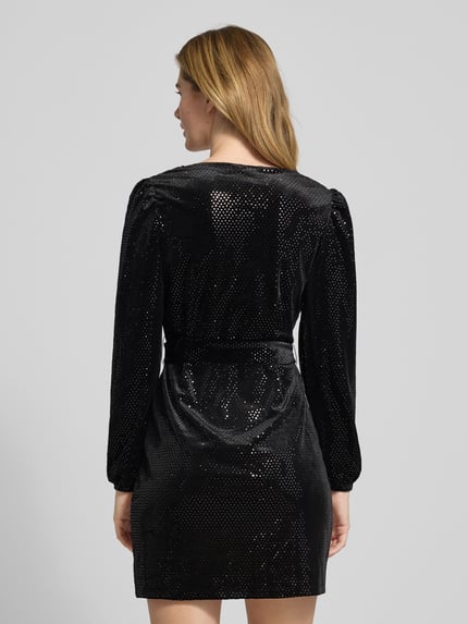 Frauenmodel trägt tailliertes Freizeitkleid mit Glitzerbesatz Modell 'SENSA' von Vero Moda, Optik: Unifarben, glänzend, Mini-Länge, V-Ausschnitt, Label-Stitching-Applikation, Gürtelband, Langarm, elastischer Ärmelabschluss, Materialverarbeitung: Samt, Ganzkörperansicht Rückansicht.
